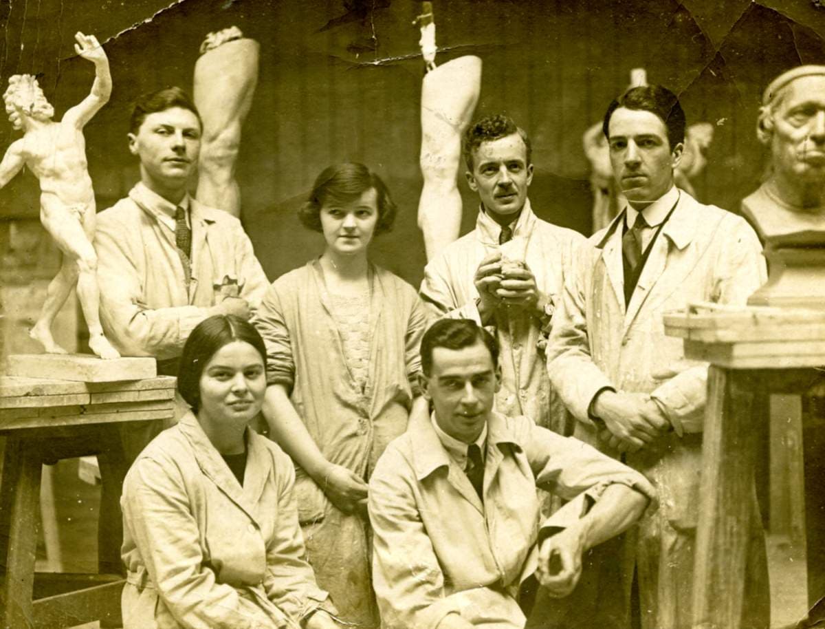 A group of people, including Barbara Hepworth, in overalls surrounded by sculptures