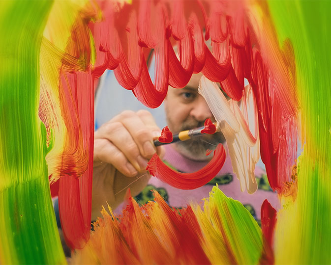Bruce Asbestos looks through glass which he is painting on with red paint